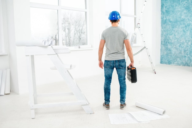 Capataz o trabajador en uniforme con instrumentos de pie en el interior blanco durante la renovación