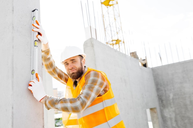 Un capataz de reparador de constructores con casco protector comprueba la uniformidad de las escaleras de una estructura de hormigón al construir una casa