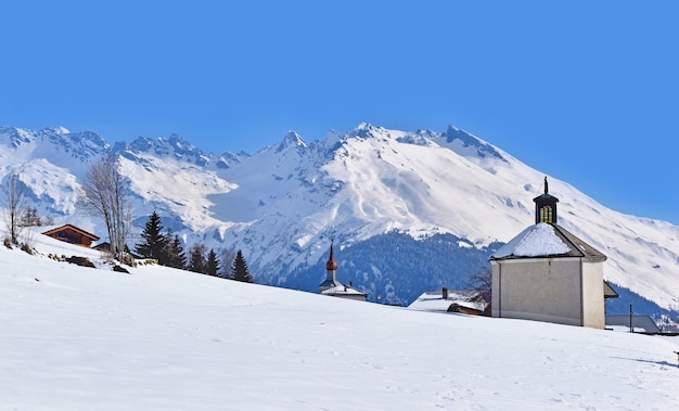 Capela em uma vila rural entre o campo e a montanha coberta de neve em inverno
