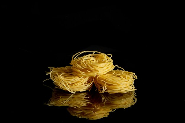 Foto capelli de pasta de huevo crudo, seco, aislado sobre fondo negro.