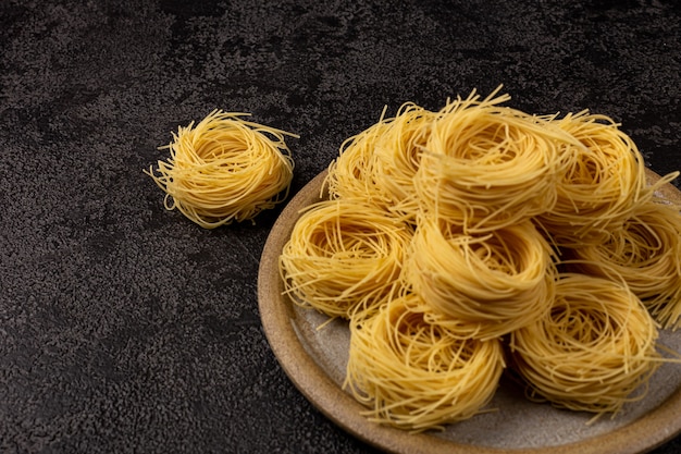 Capellini-Spaghetti auf einer Keramikplatte auf dunklem strukturellem Hintergrund mit Platz zum Kopieren von Spaghetti