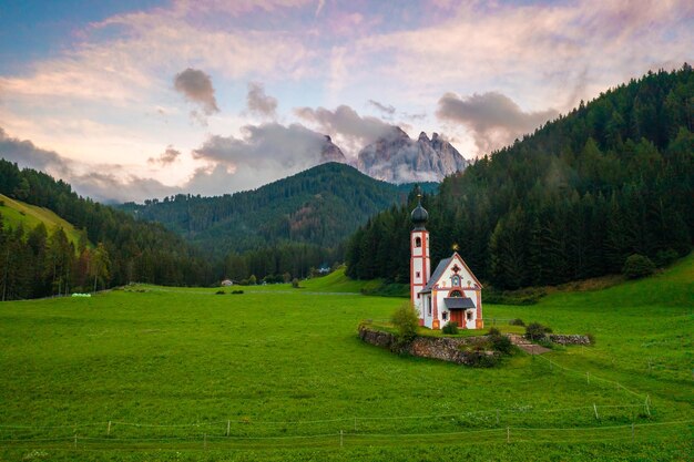 Capilla de St Johann en Tirol del Sur contra los Dolomitas cubiertos por nubes al atardecer