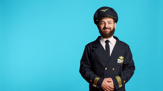 Capitán de avión masculino con uniforme de aerolínea y posando en el estudio, con ocupación profesional. Adulto joven que trabaja como piloto para volar un avión, siendo alegre y positivo en cámara.