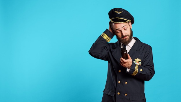 Capitán de la tripulación aérea mirando botellas de vitaminas, sintiéndose inseguro acerca de los suplementos y el tratamiento médico. Joven piloto sosteniendo frascos de pastillas y medicamentos, profesión de aviador.