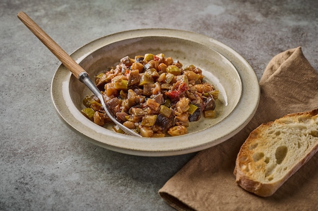 Caponata siciliana tradicional caseira com berinjela, abobrinha, tomate, azeitonas e pão ciabatta. Close up, copie o espaço