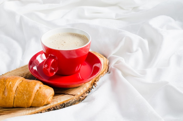 Cappuccino, chocolate e croissant em uma cama.