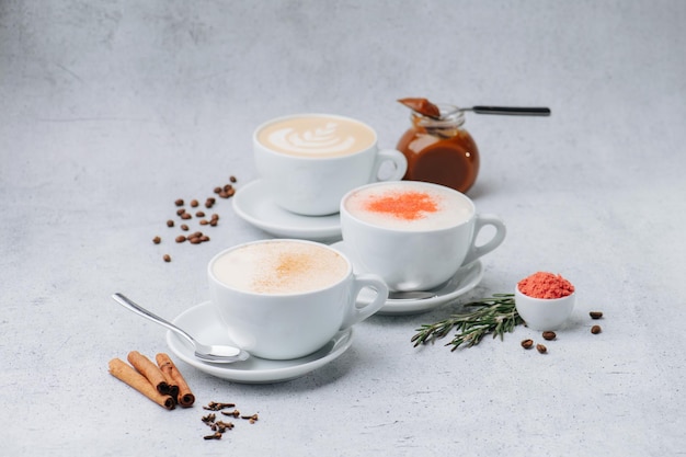 Cappuccino com creme e especiarias em três xícaras em pires em uma superfície de mesa