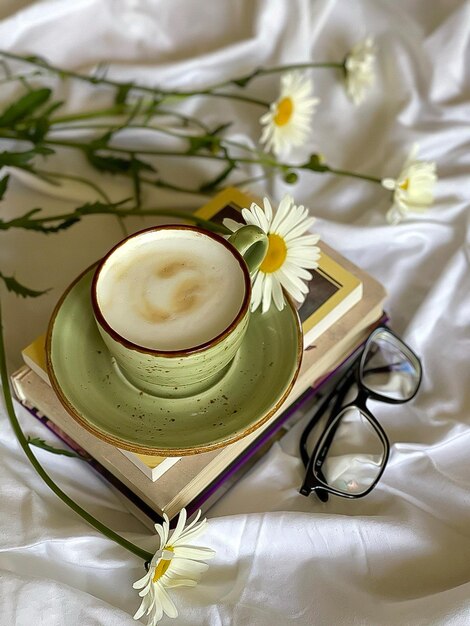 cappuccino em um lençol branco com margaridas, café em uma caneca cor de pistache em livros, foto no telefone