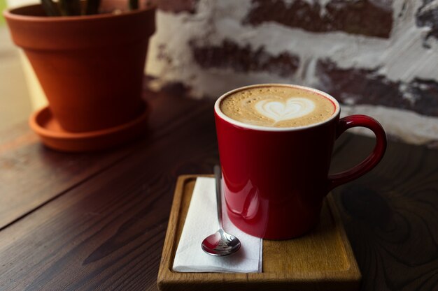 Cappuccino em uma caneca vermelha em uma mesa de madeira