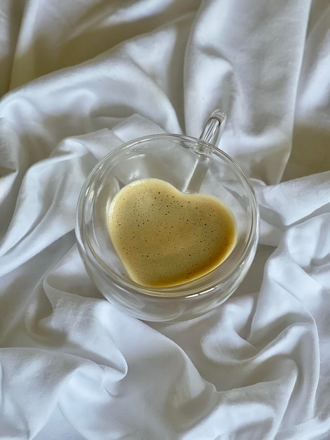 Cappuccino in einem herzförmigen Glasbecher auf einem weißen Blatt, Morgenkaffee, Foto am Telefon