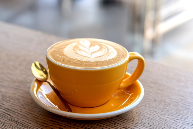 Cappuccino in gelber Kappe mit Latte Art auf einem Holztisch