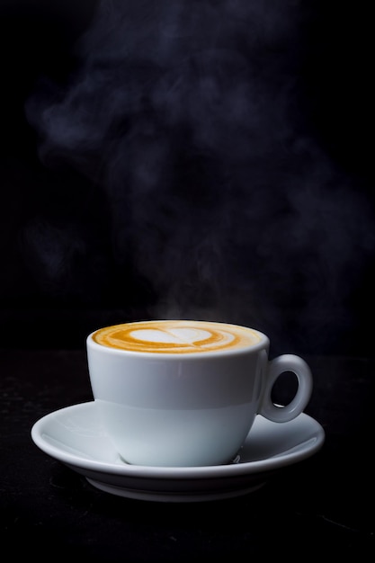 Cappuccino mit Dampf und Herz lieben Latte Art in weißer Tasse auf dem schwarzen Tisch