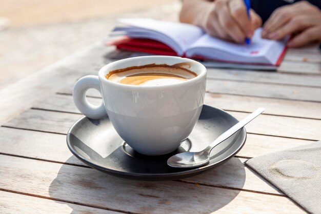 Foto cappuccino mit süßem schaum in einem keramikbecher mit schwarzer untertasse auf einem holztisch frühstück im freien