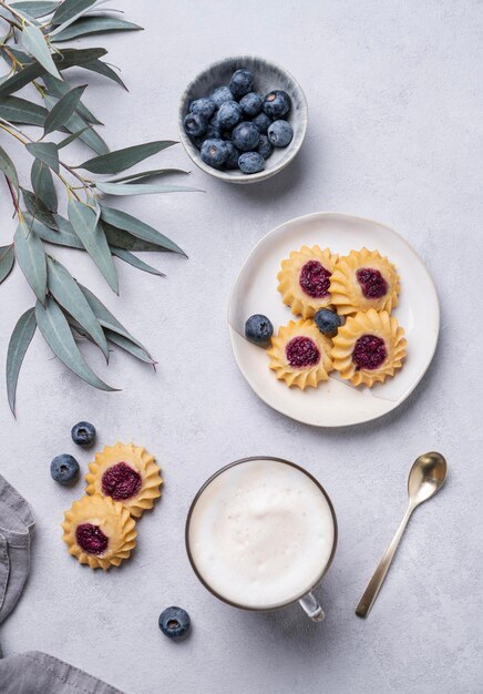 Cappuccino ou latte com espuma de leite em uma xícara com biscoitos caseiros de baga e mirtilos sobre um fundo claro com ramos de eucalipto Conceito café da manhã de primavera