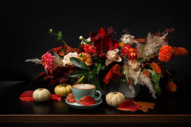 Cappuccino und schöne Blumen Stillleben. Blumenladen Zusammensetzung. Kaffeetasse mit Schaum, Apfel, frischem und getrocknetem Blumenstrauß auf schwarzem Holztisch. Floristische Kunst und Blumenmusterkonzept