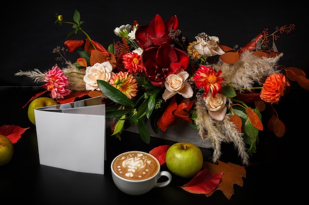 Cappuccino und schöne Blumenzusammensetzung. Blumenladen Zusammensetzung. Kaffeetasse mit Schaum, Apfel, frischem und getrocknetem Blumenstrauß auf schwarzem Holztisch. Floristische Kunst und Blumenmusterkonzept