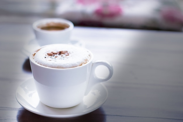 Cappuccinokaffee mit Kakao belegt in der weißen Schale im Café mit Morgentageslicht.