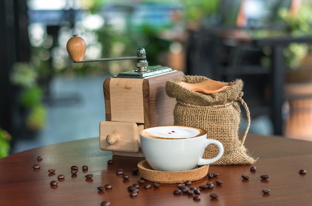 Cappuccinokaffeetasse auf hölzerner Tabelle mit traditionellen Kaffeebohnen und Schleifer