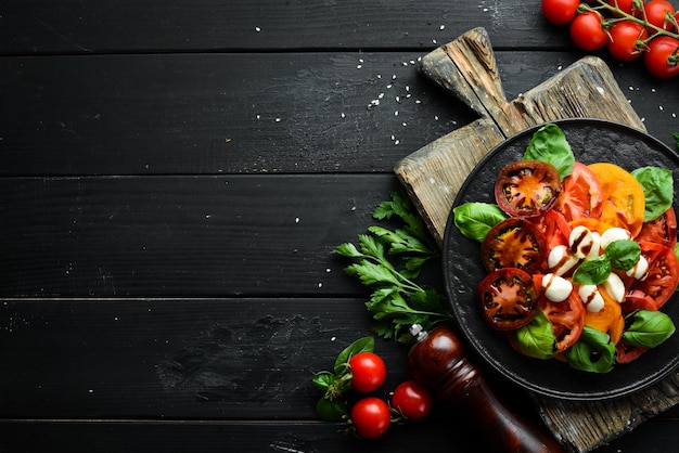 Caprese-Salat auf einem schwarzen Teller. Tomaten, Mozzarella und Basilikum. Ansicht von oben. Freiraum für Ihren Text.