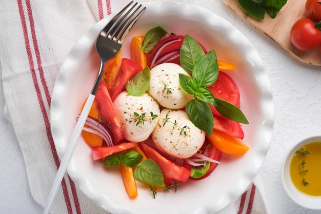 Caprese-Salat Italienischer Caprese-Salat mit in Scheiben geschnittenen Tomaten Mozzarella-Käse-Basilikum-Olivenöl in weißen Teller auf weißem Hintergrund Leckeres italienisches Essen Draufsicht Rustikaler Stil