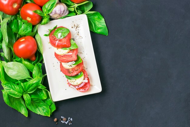 Caprese-Salat mit Mozarellakäse, Tomaten und Basilikum auf Platte. Schwarzer Hintergrund und Exemplarplatz