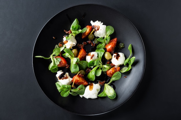 Caprese-Salat mit Mozzarella, Tomate, Basilikum und Balsamico-Essig auf schwarzem Teller angeordnet