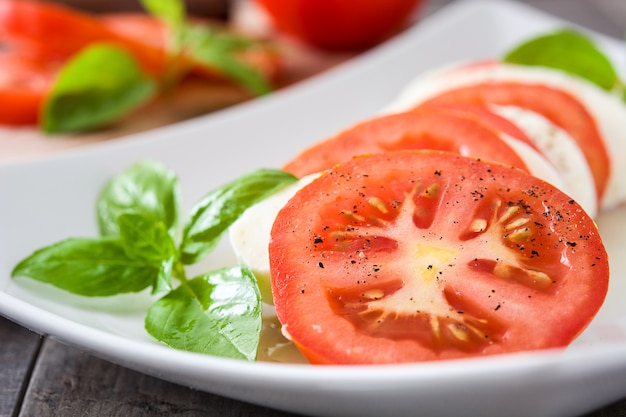 Caprese-Salat mit Mozzarellakäsetomaten und -basilikum auf rustikalem Holztisch