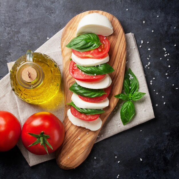 Caprese-Salat, Mozzarella-Käse, Tomaten und Basilikumblätter auf dem Schneidbrett über einem Steintisch