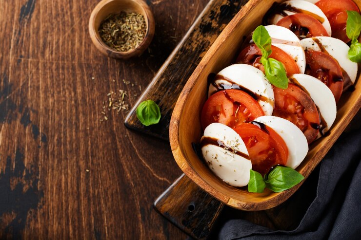 Foto caprese traditioneller italienischer salat in olivenholzschale auf alter rustikaler oberfläche