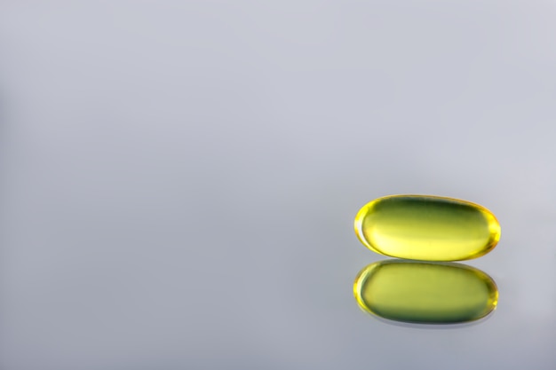 Foto cápsula gelatinosa de color amarillo sobre fondo gris. salud. vitaminas d, e, omega 3. espacio de copia
