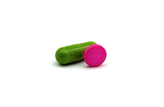 Una cápsula medicinal verde y una tableta rosa se cierran.