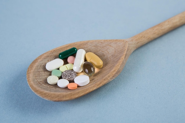 Cápsula de tableta de píldoras y vitamina en cuchara de madera sobre medicina de fondo azul y concepto de droga