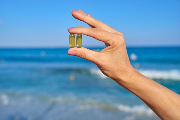 Cápsula de vitamina d, e, a, omega 3, aceite de pescado en primer plano de la mano. Mar azul, fondo de cielo. Alimentación saludable, medicina, estilo de vida, concepto de suplementos nutricionales