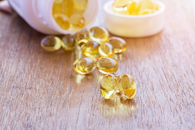 Foto cápsulas de aceite de hígado de pescado omega 3 en fondo de madera pila de grandes pastillas doradas translúcidas en pequeñas