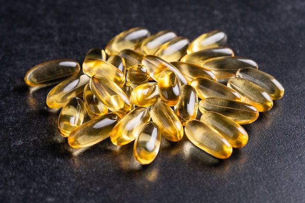 Foto cápsulas de aceite de pescado amarillo, omega 3, sobre un fondo negro