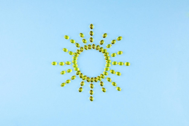Cápsulas amarillas con vitamina D3 en forma de sol con rayos sobre un fondo azul concepto saludable y médico de vitamina del sol