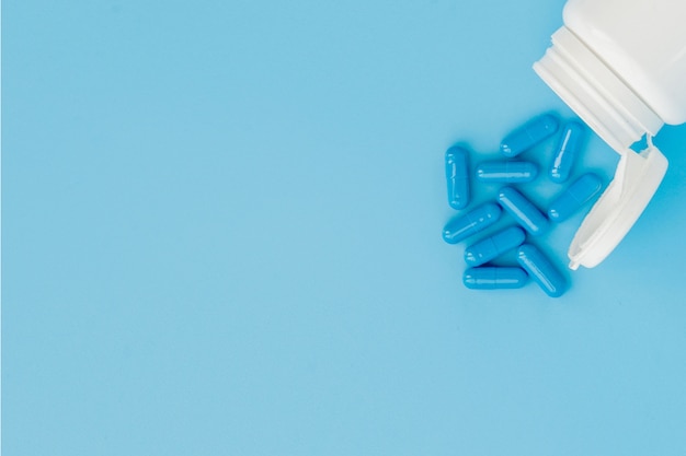 Cápsulas azules, píldoras sobre un fondo azul. Cápsulas en un frasco blanco. Vitaminas, suplementos nutricionales para la salud de la mujer.