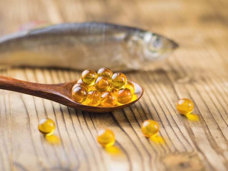 Cápsulas de óleo de peixe em uma colher de pau em uma mesa de madeira com um peixe no fundo Foco seletivo