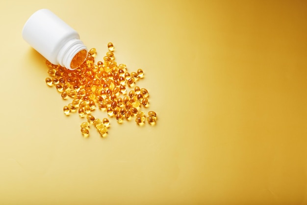 Cápsulas de vitamina d3 de ouro derramadas de um frasco em um fundo amarelo com espaço livre a vitamina mais importante em uma forma líquida facilmente digerível