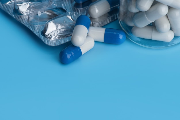 Cápsulas dos comprimidos da medicina na bolha e na garrafa em um fundo azul com espaço da cópia.
