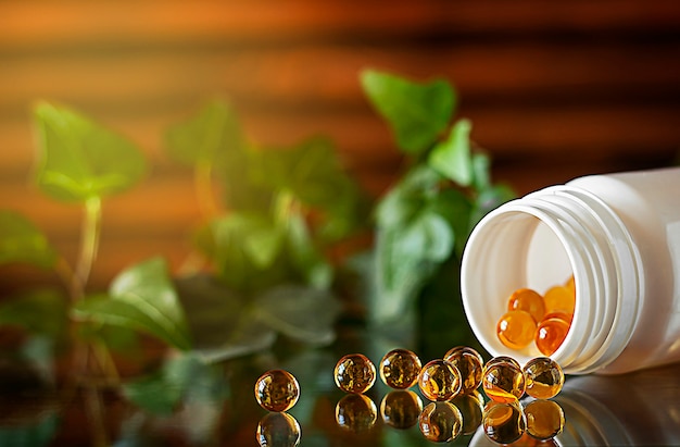 Cápsulas de gel de vitamina D3 amarillas se esparcen desde la burbuja Reflejada en la superficie del vidrio En el fondo hay un frasco blanco abierto con cápsulas llenas de cápsulas Espacio de copia Fondo de madera y