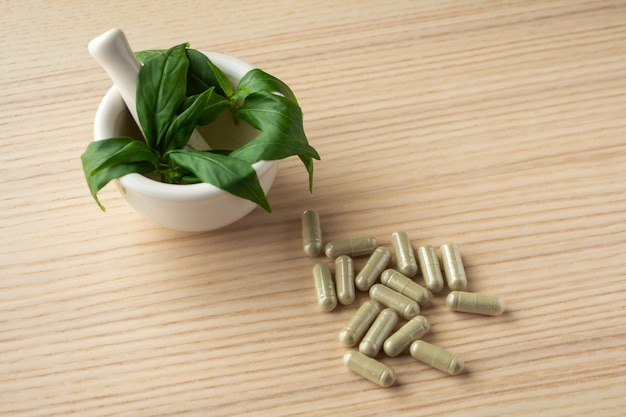 Cápsulas de hierbas medicinales con hoja de Andrographis paniculata sobre mesa de madera