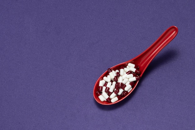 Cápsulas de píldora de medicina farmacéutica, en cuchara de plástico rojo sobre fondo púrpura.