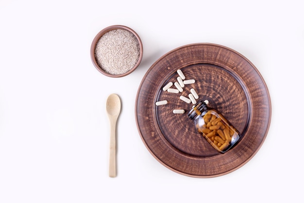 Cápsulas de psyllium en un frasco de vidrio sobre un plato y cáscara de psyllium en una taza