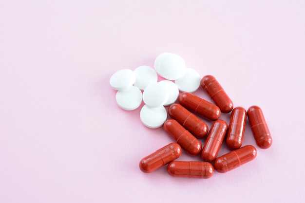 Cápsulas rojas y pastillas blancas en un primer plano aislado de fondo rosa
