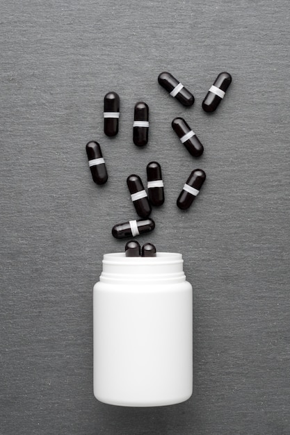 Las cápsulas de suplemento negro se vierten de una botella blanca. Vista superior, endecha plana. Tema de medicina, concepto de salud.