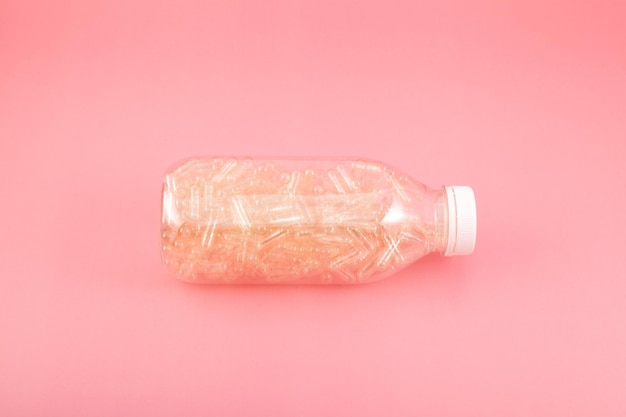 Cápsulas vacías de gelatina natural en botella de plástico sobre fondo rosa