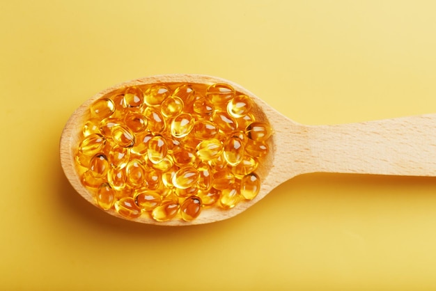 Cápsulas de vitamina D3 en una cuchara con otras cápsulas de vitamina D3 a su alrededor sobre un fondo amarillo Cápsulas viejas con un suplemento dietético para articulaciones, dientes y huesos Espacio libre de primer plano