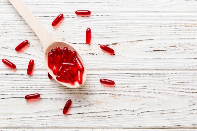 Cápsulas de vitaminas en una cuchara sobre un fondo de color Píldoras servidas como una comida saludable Capsulas de suplementos vitamínicos de gel blando rojo en cuchara