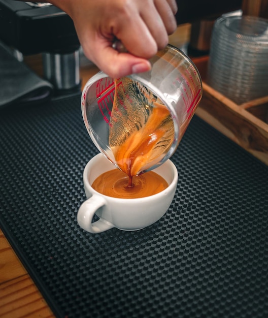 Captura aproximada da mão do barista derramando café expresso em xícara medidora na xícara de café